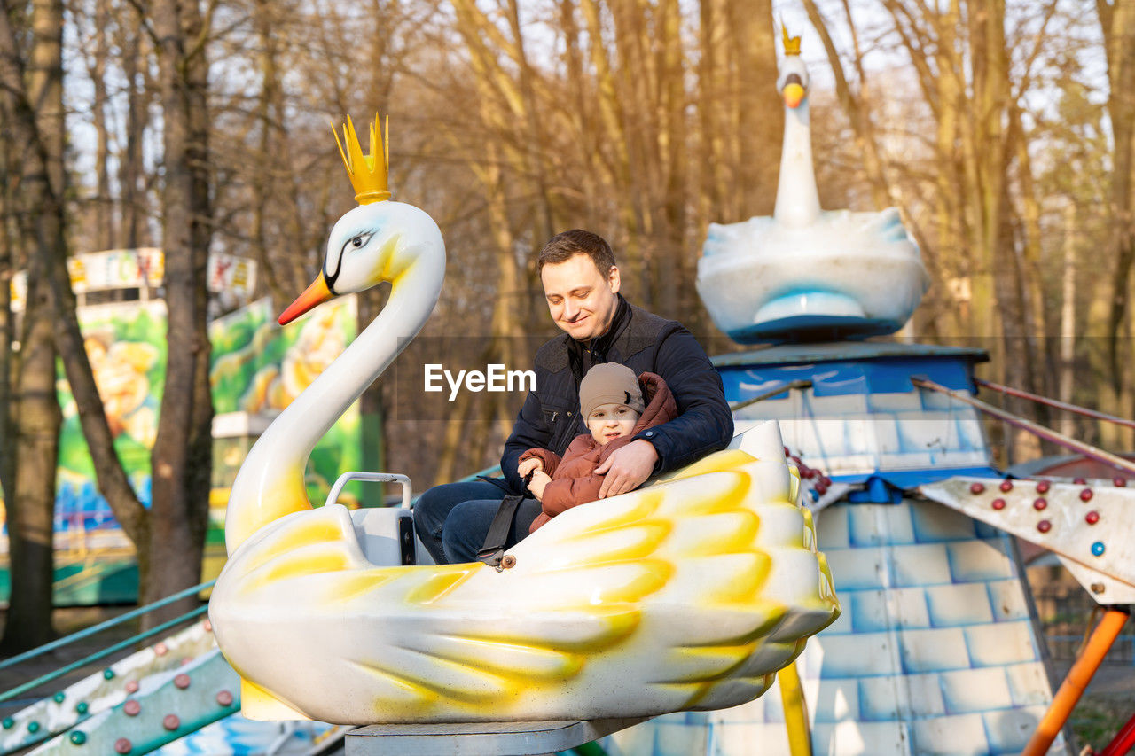 Happy dad and son ride on attractions in a city park on a sunny day. spending time with family.