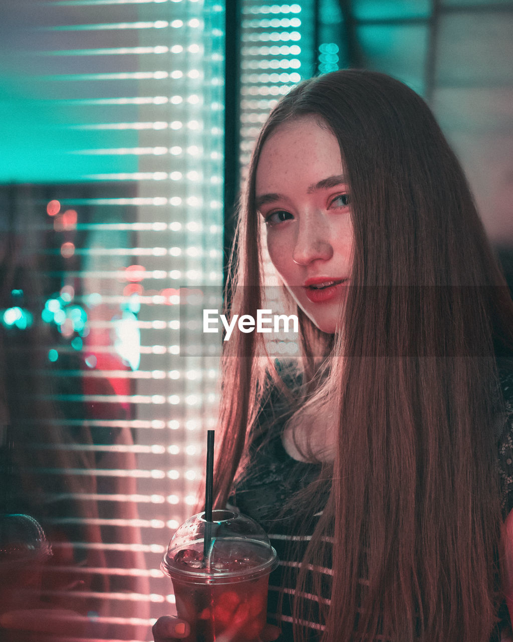 Portrait of young woman having drink against window