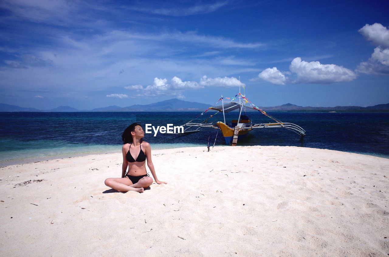 Young woman sitting by sea against sky