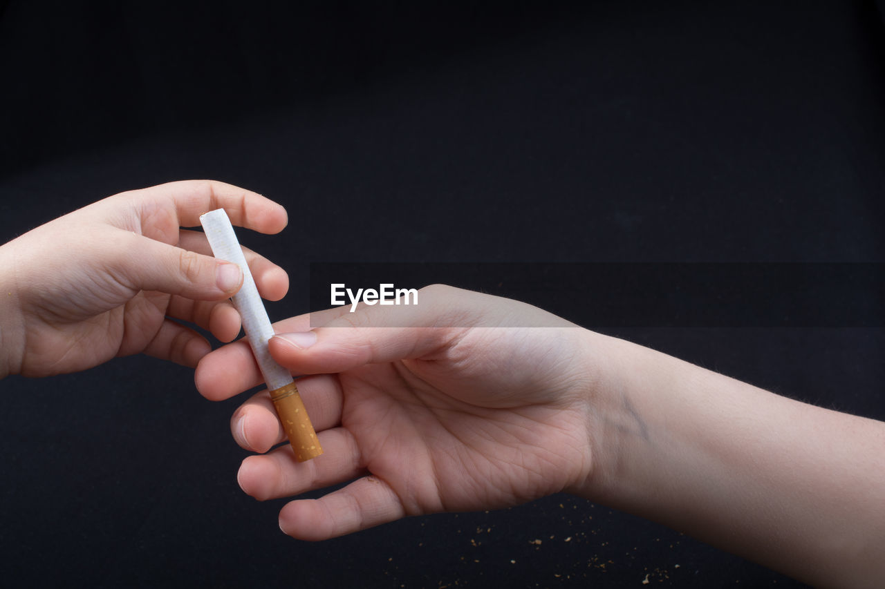 Close-up of person hand giving cigarette to child over black background