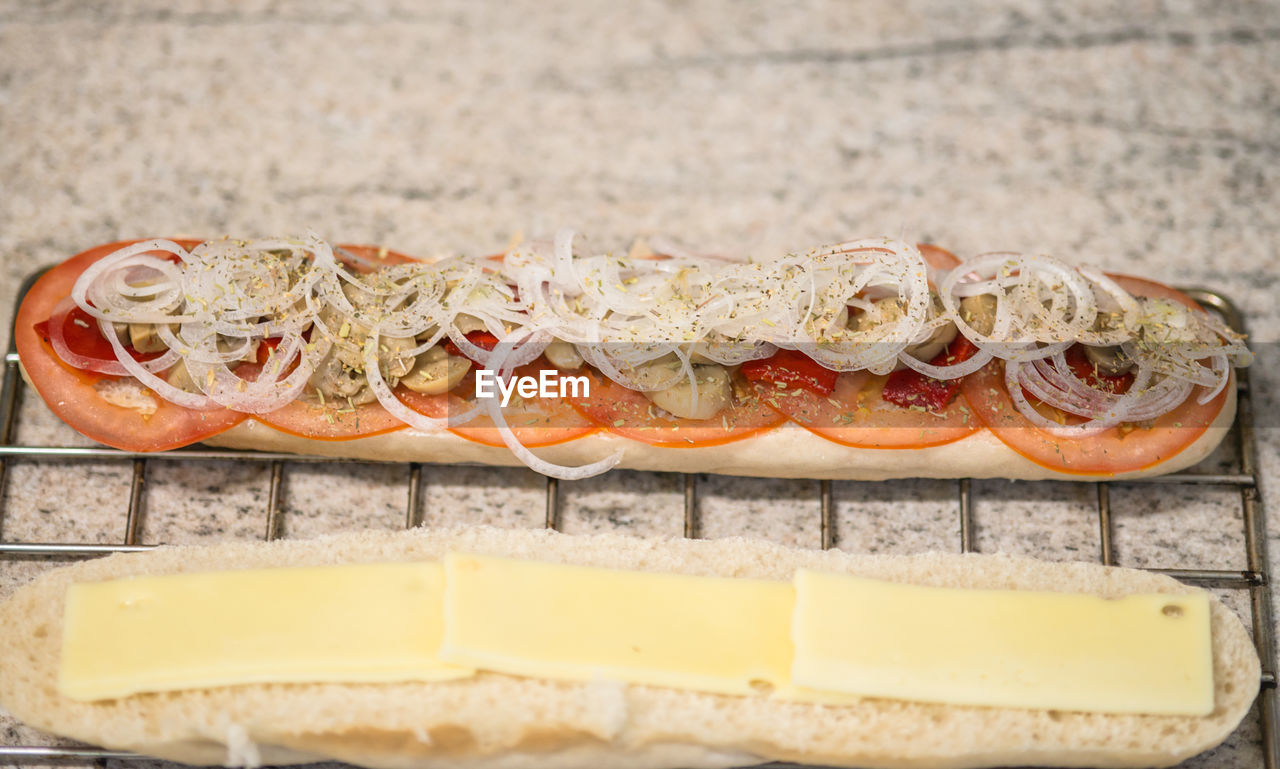 High angle view of vegetable slices and cheese on baguette at table