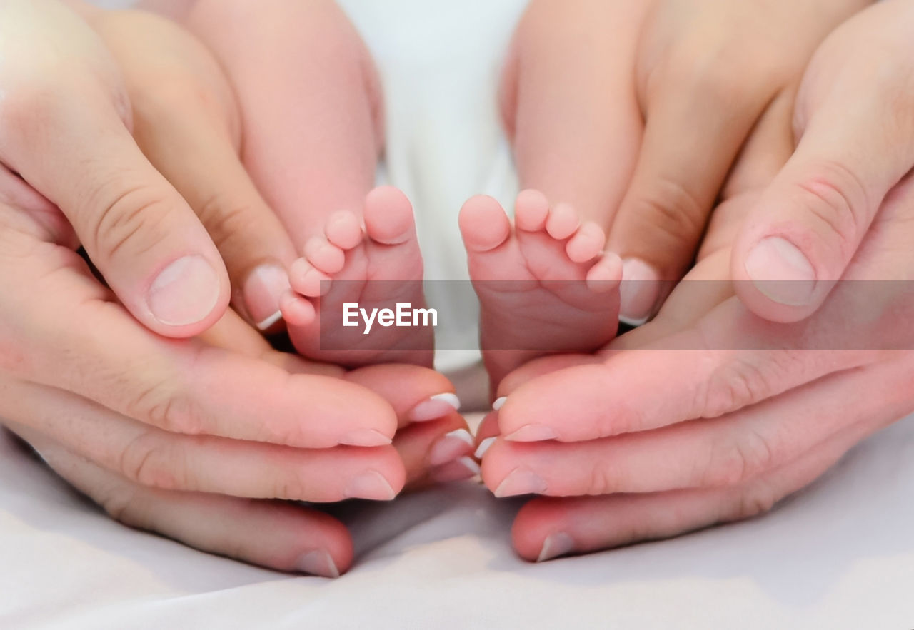 Cropped hands of parents holding baby legs