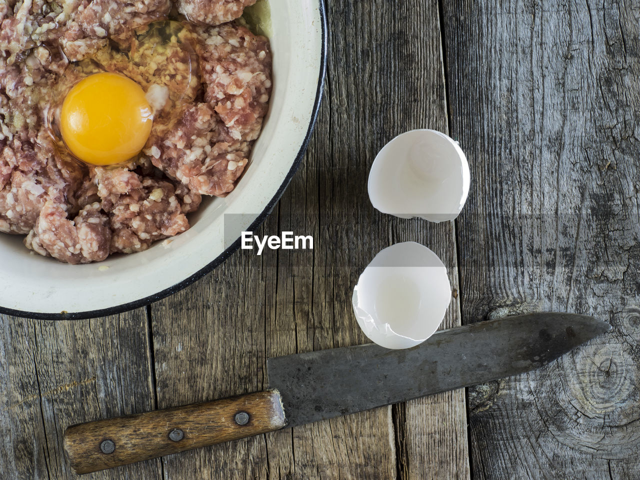 Directly above shot of minced meat with egg yolk in bowl by knife on table