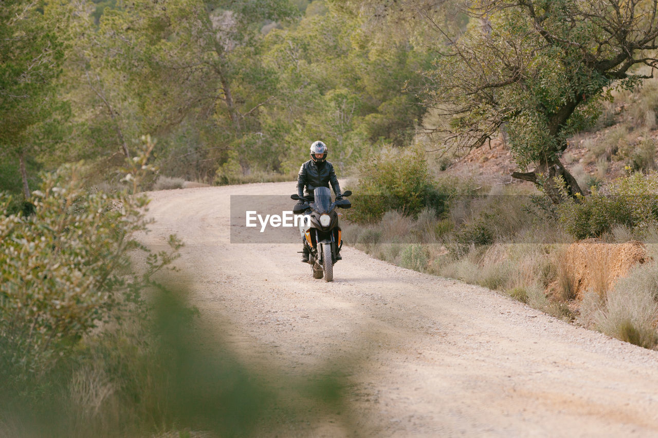 FULL LENGTH OF MAN RIDING MOTORCYCLE ON DIRT ROAD