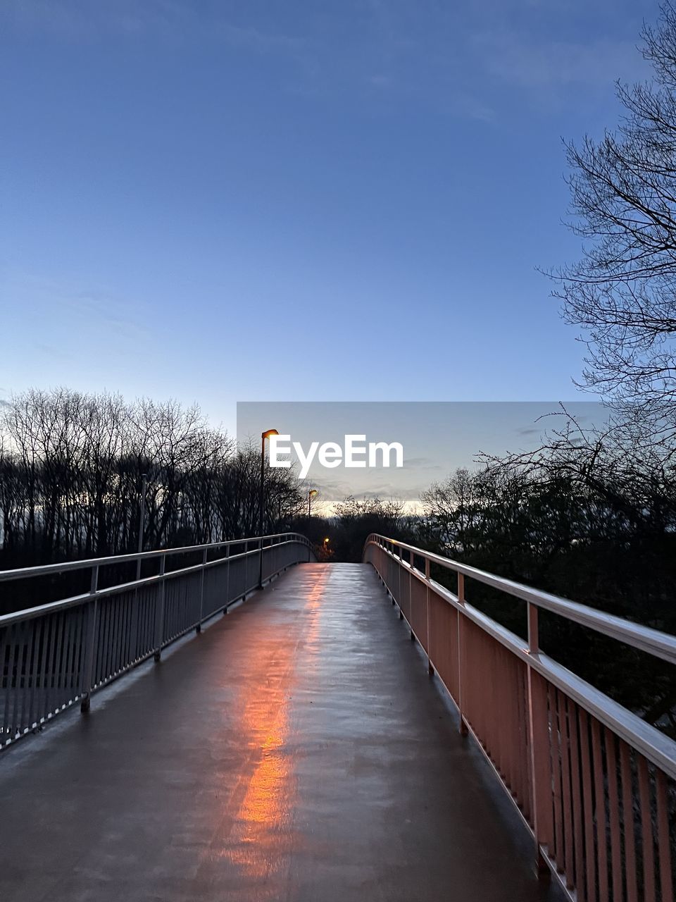 reflection, sunlight, light, transportation, rail transportation, railroad track, track, sky, nature, mode of transportation, blue, architecture, train, morning, public transportation, line, no people, tree, outdoors, darkness, transport, built structure, travel, vehicle, day, motion, plant, diminishing perspective