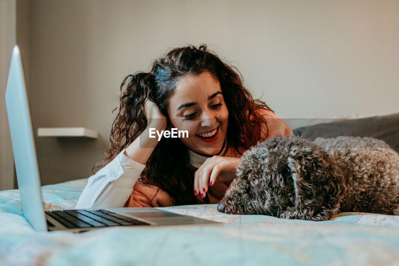 Smiling young woman with dog sitting on bed at home