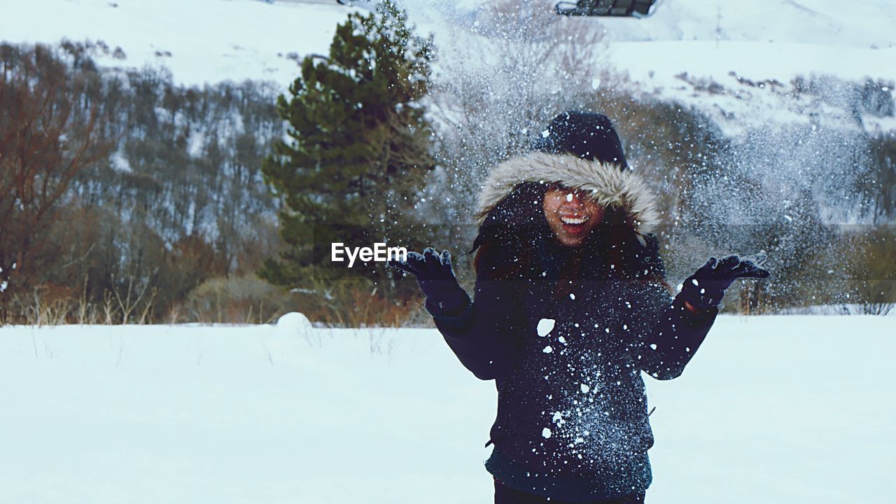 Cheerful woman throwing snow against trees