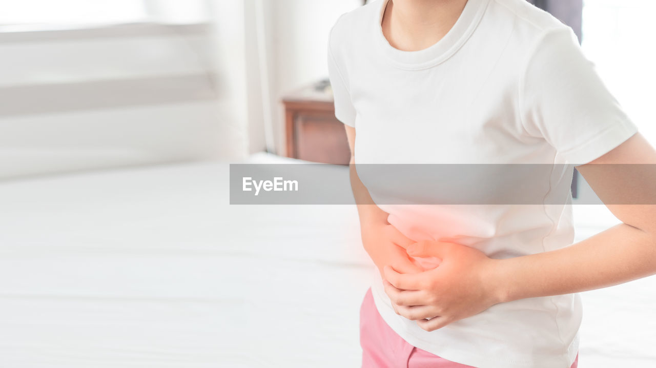 MIDSECTION OF WOMAN STANDING AGAINST WALL AT HOME