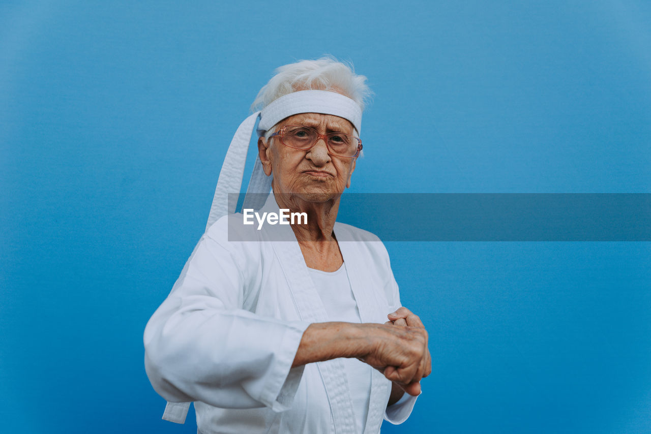 Portrait of senior woman doing karate against blue background