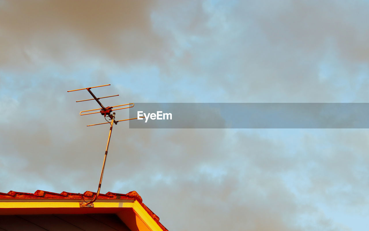 Low angle view of television aerial on house roof against sky