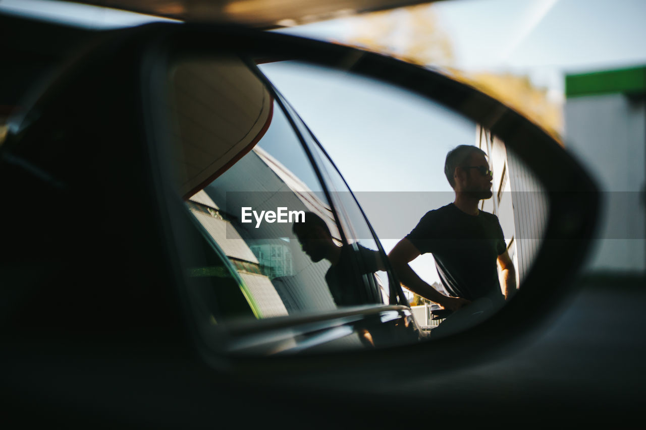 Reflection of man on side-view mirror of car