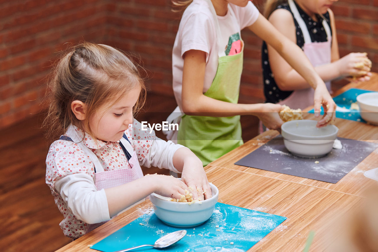 High angle view of girls kneading dough in bowl on table