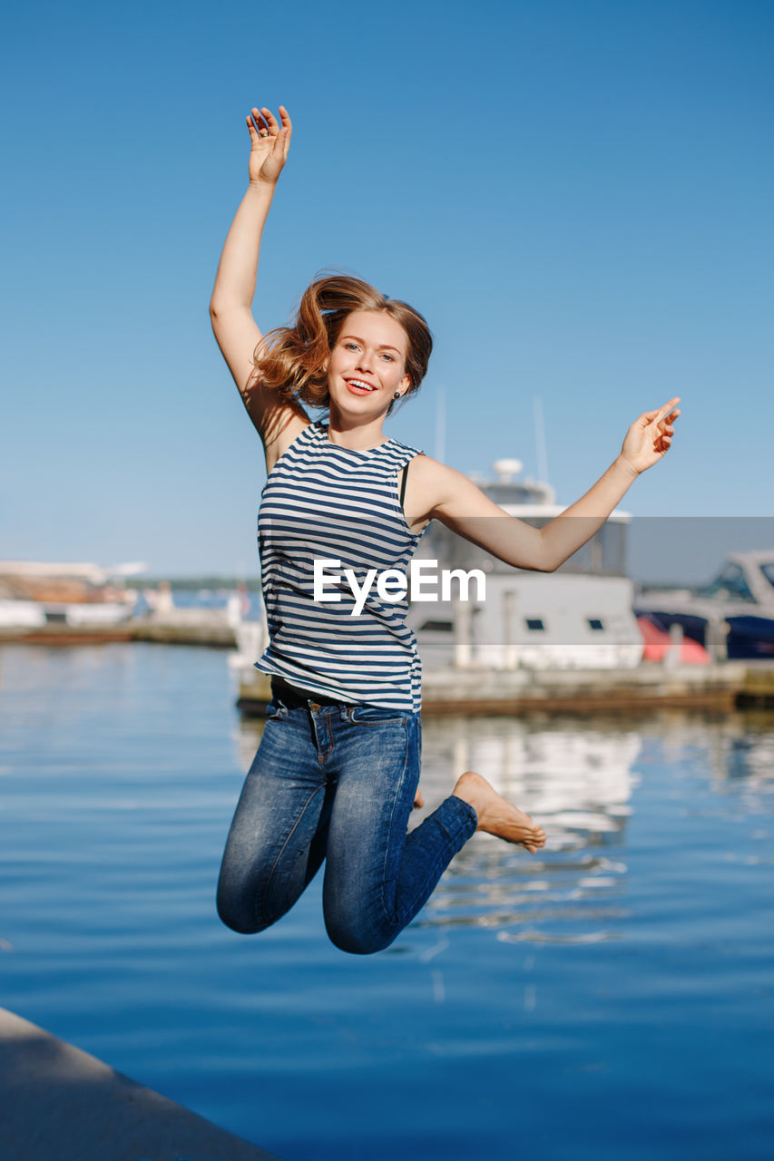 Portrait of smiling young woman jumping at harbor
