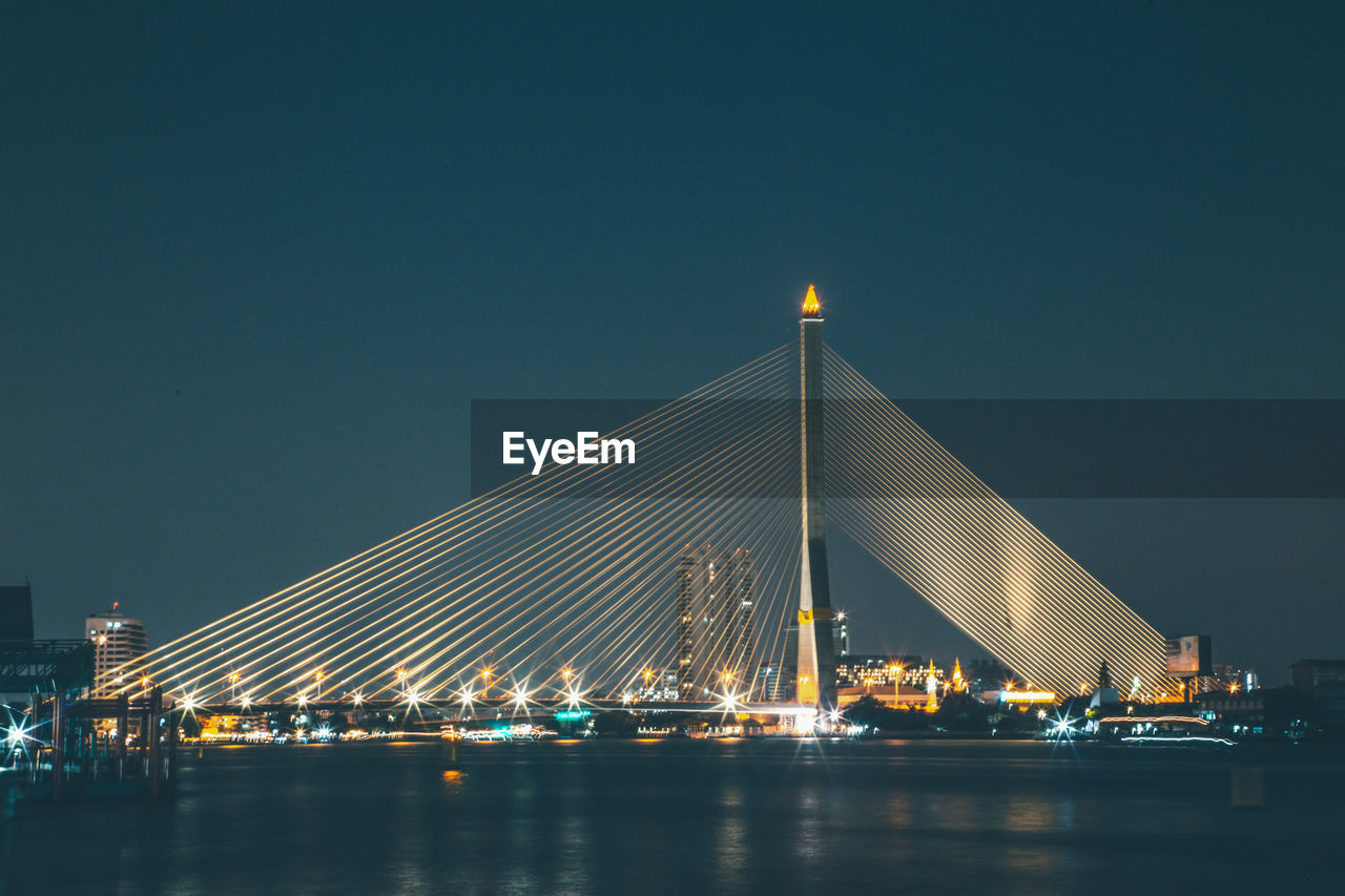 Illuminated bridge over river against sky at night