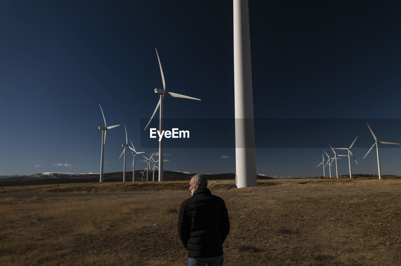 Adult man in winter cloth with modern windmills against blue sky. shot in castilla la mancha, spain