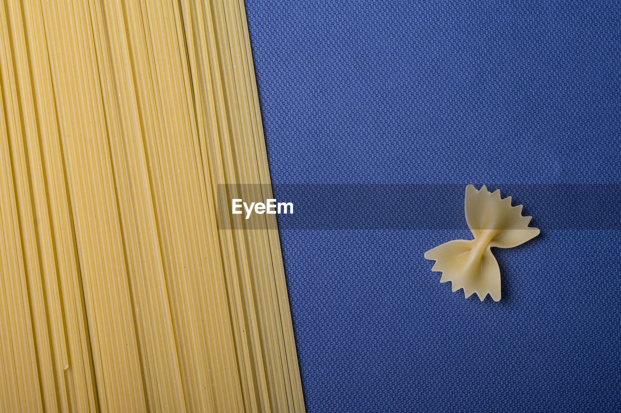 Spaghetti strands and a single farfalle pasta on blue paper. food background texture, top view