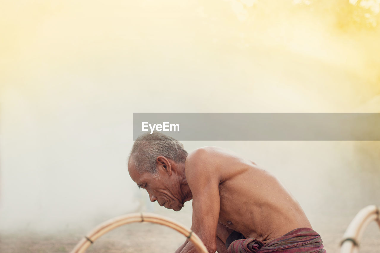 Shirtless senior man making straw basket