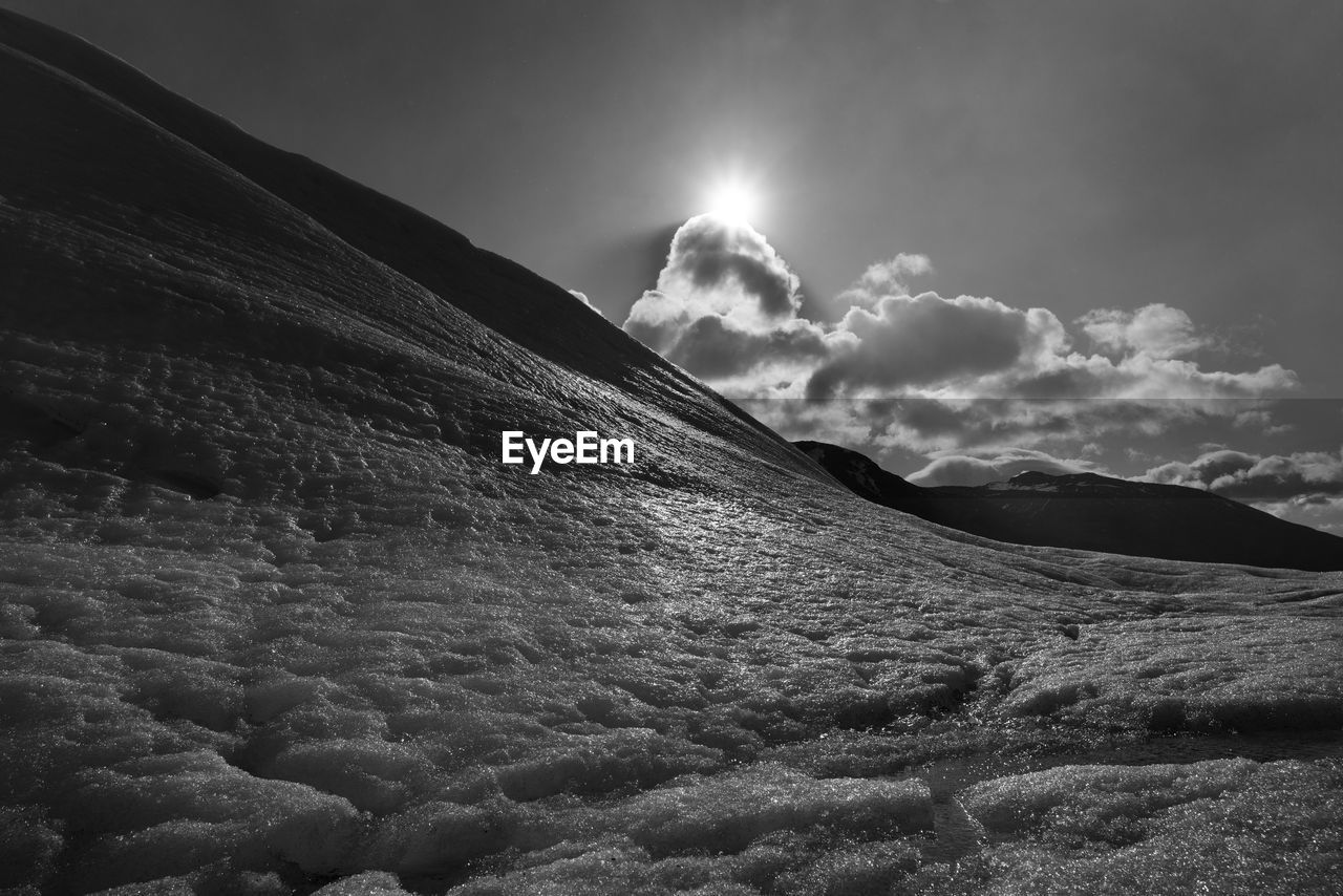LOW ANGLE VIEW OF MOUNTAINS AGAINST BRIGHT SUN