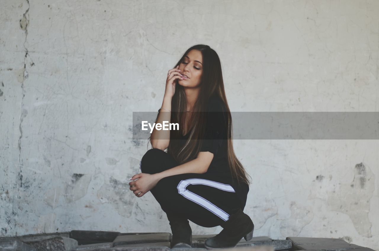 Beautiful woman with long hair crouching by wall