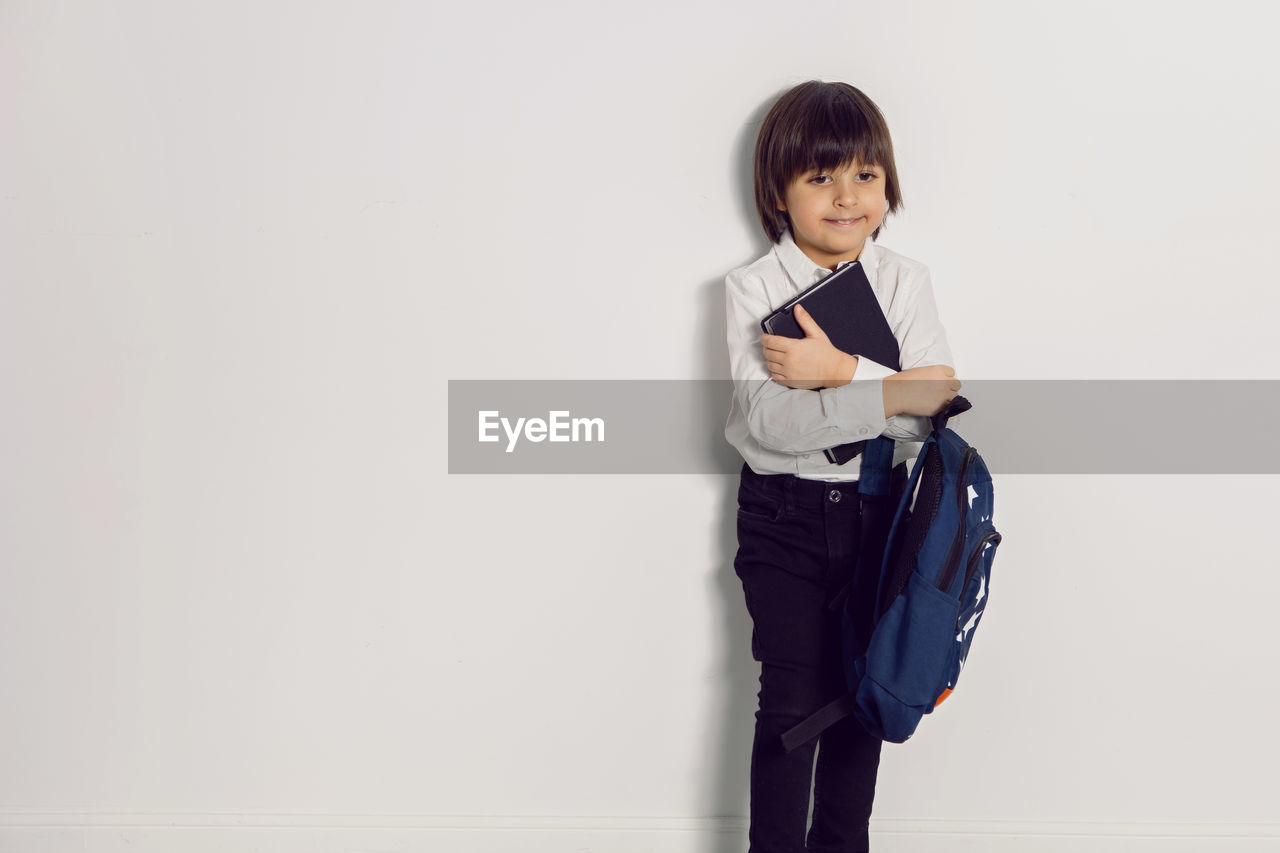 Child boy with a book textbook and backpack stands on a white background