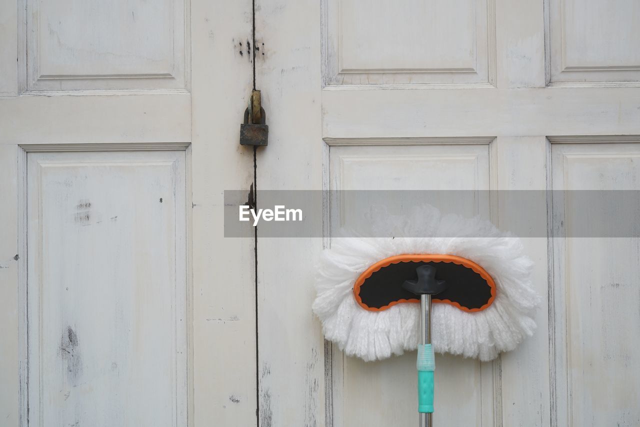 A white mop placed standing on the white vinatge door.