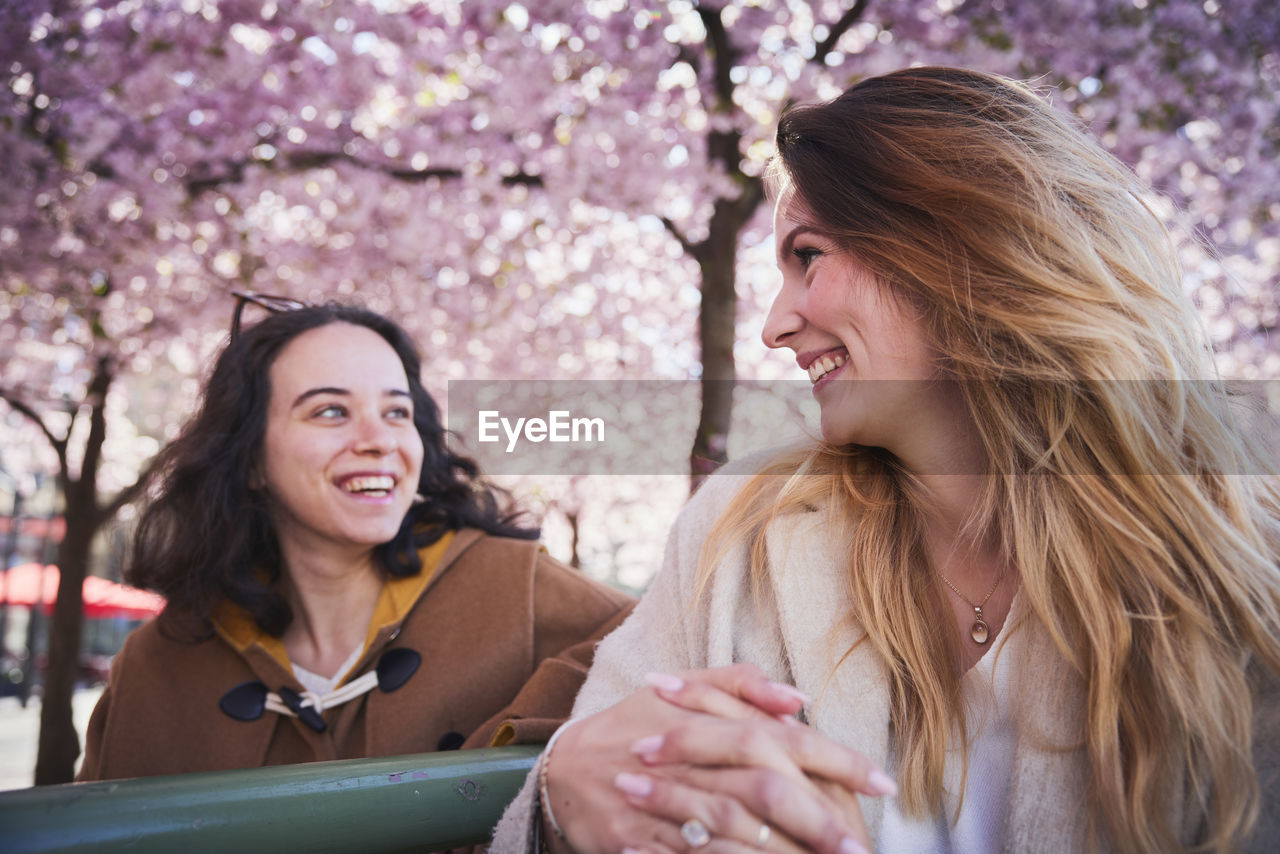 Smiling young women standing under cherry blossom