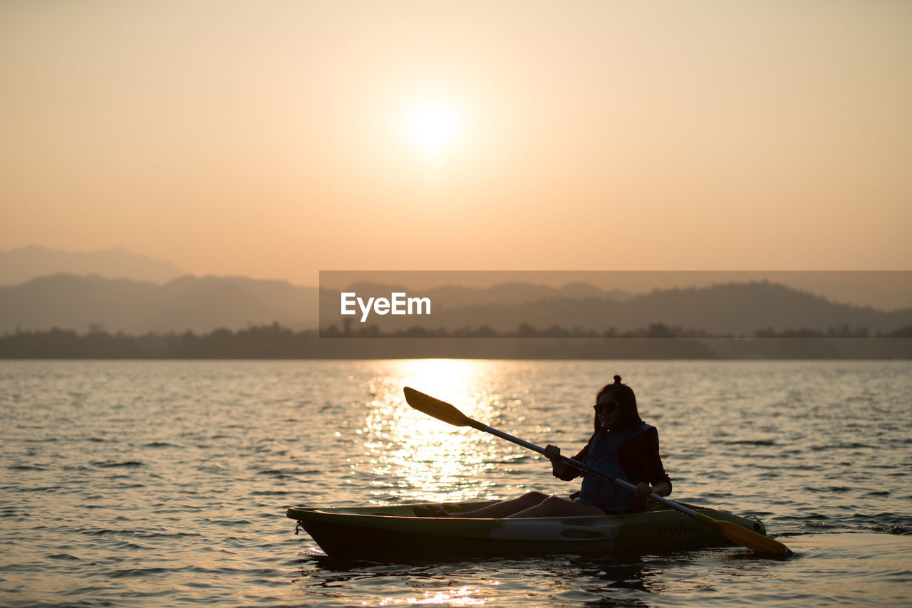 Woman boating on lake during sunset