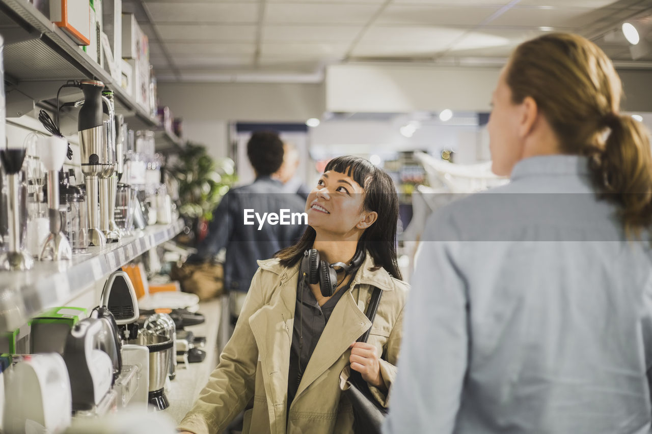 Young customer looking at appliances while standing by mature female owner in store