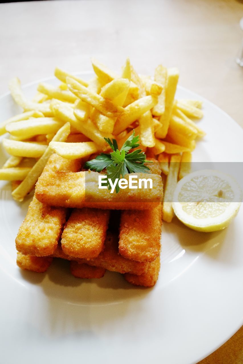 High angle view of fish fingers with french fries served in plate on table