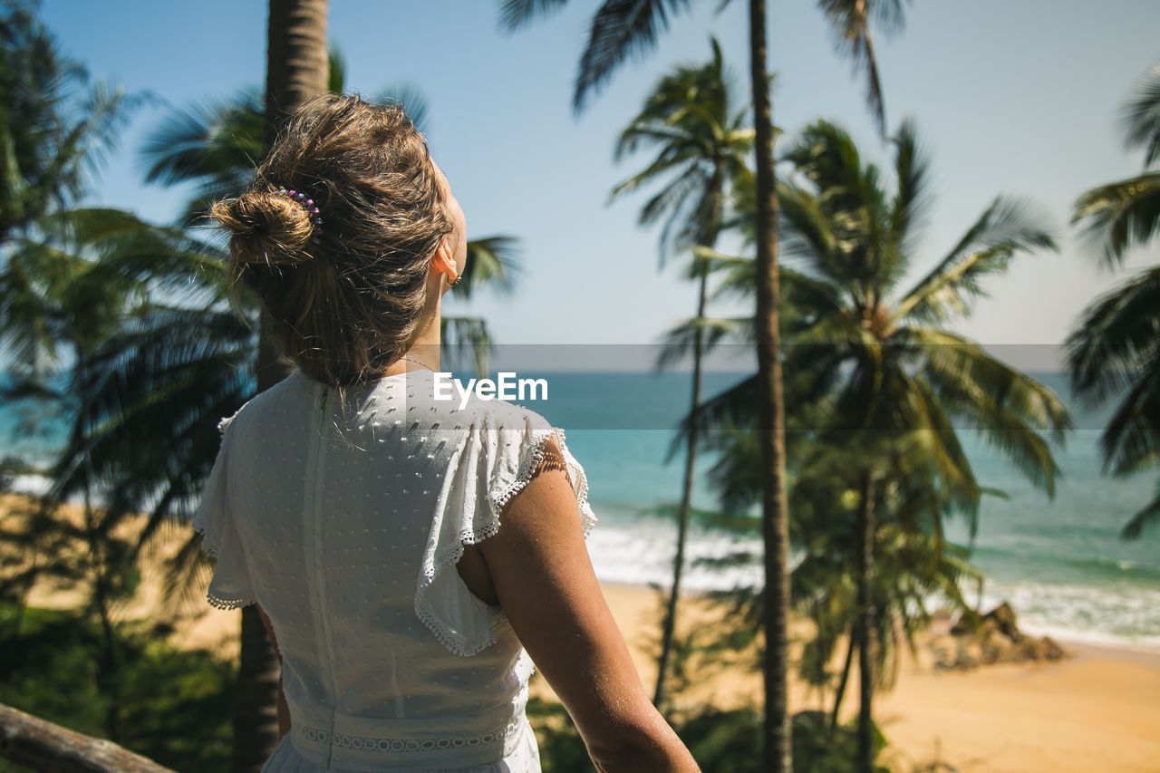 Rear view of woman standing by palm tree at beach