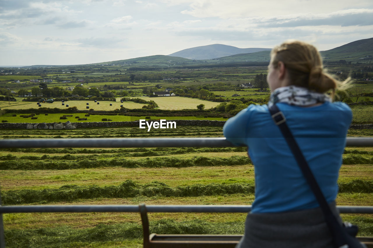 REAR VIEW OF WOMAN STANDING IN FARM AGAINST SKY