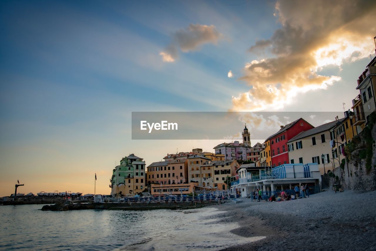 Buildings by sea against sky during sunset