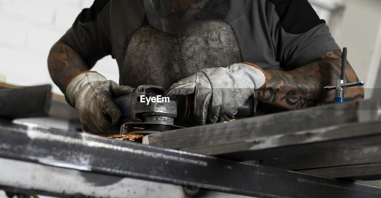 Side view of male welder using electric grinder and cutting metal detail in grungy workshop
