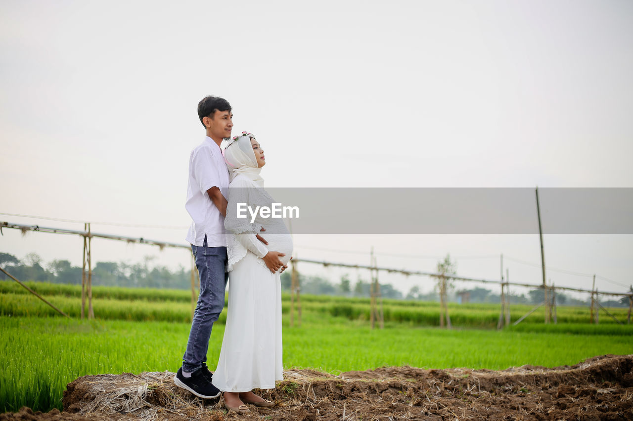 Full length of young man and pregnant woman standing on field