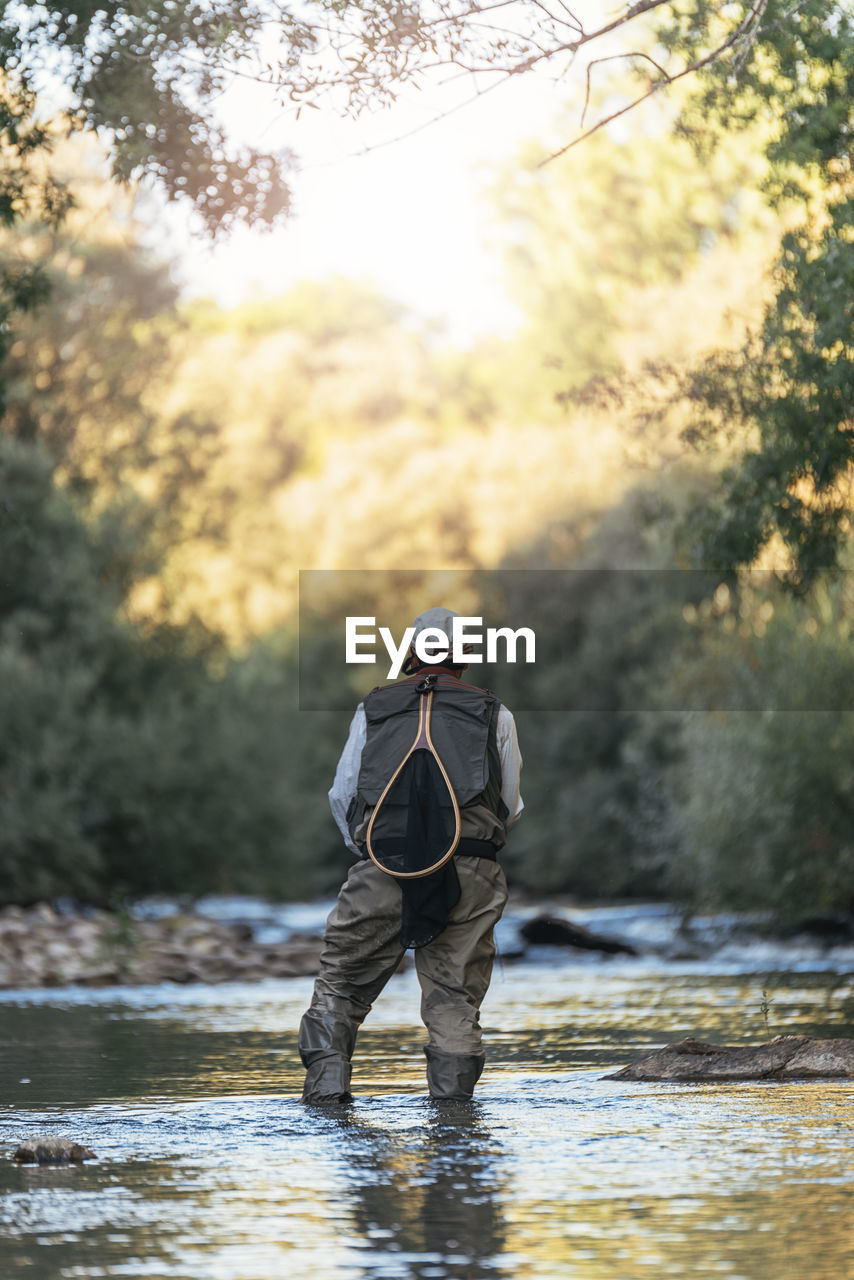 REAR VIEW OF MAN IN RIVER AGAINST FOREST