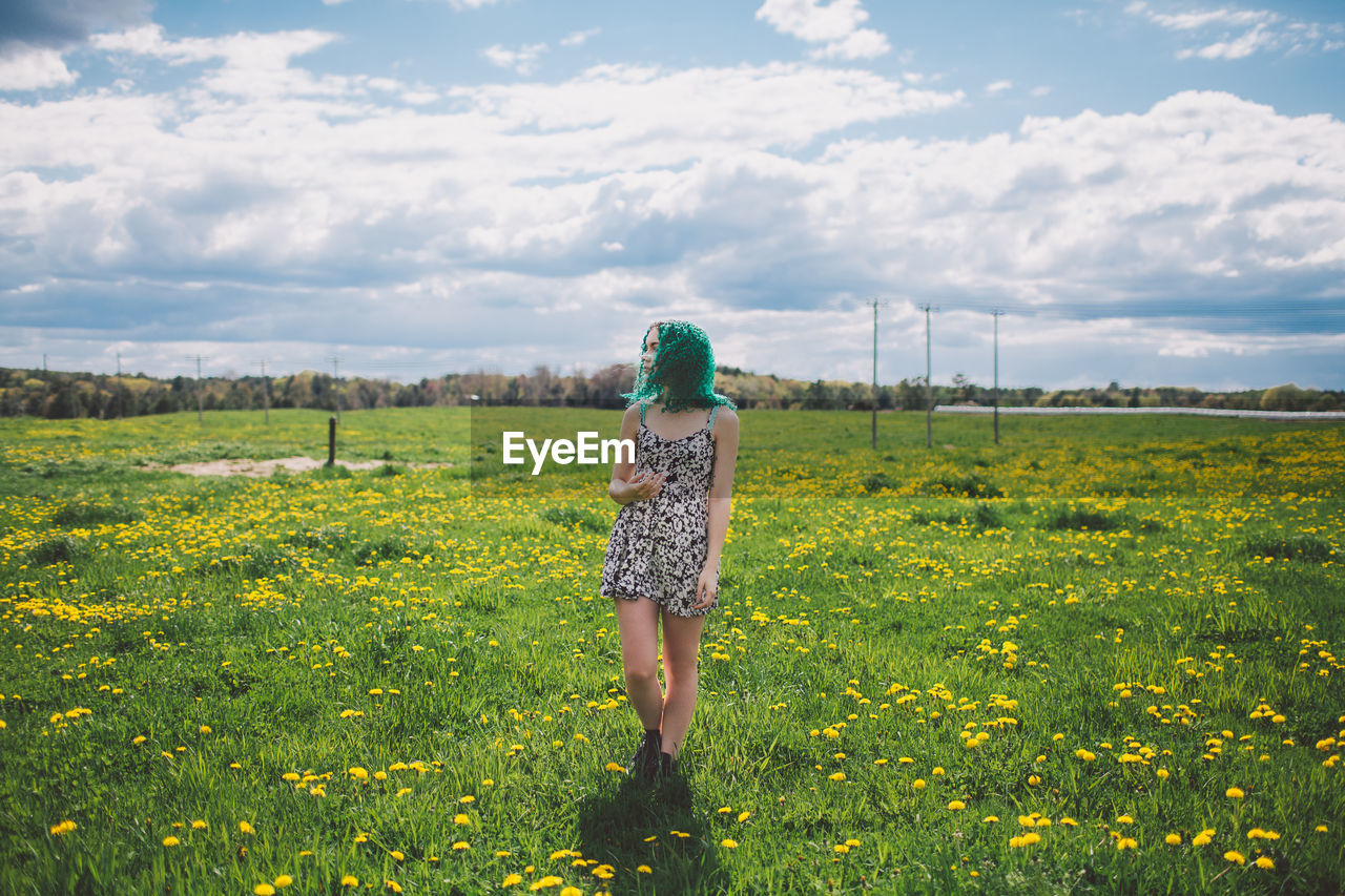 Full length of woman standing on yellow flowers field against cloudy sky