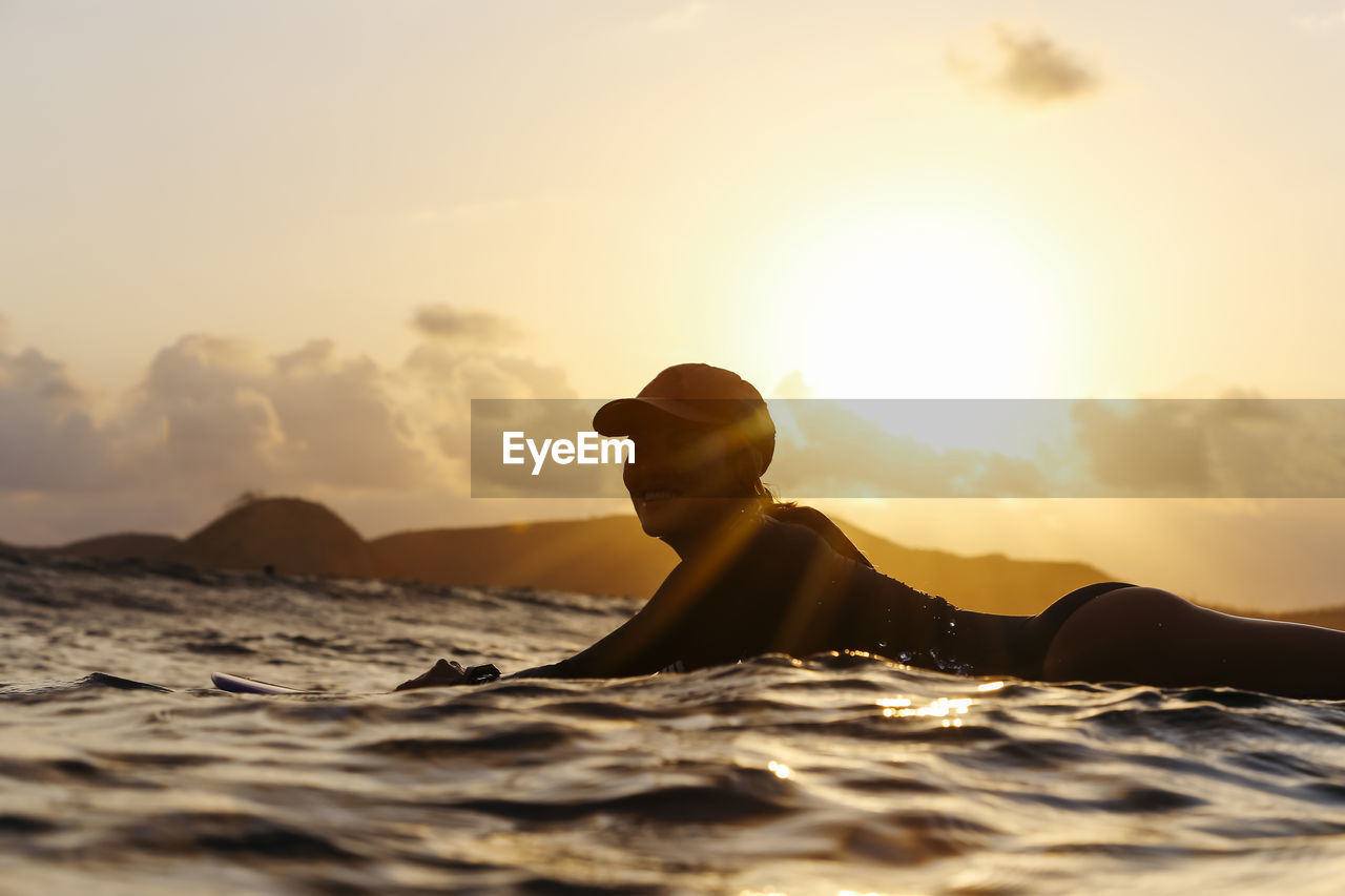 Female surfer lying on surfboard in the evening