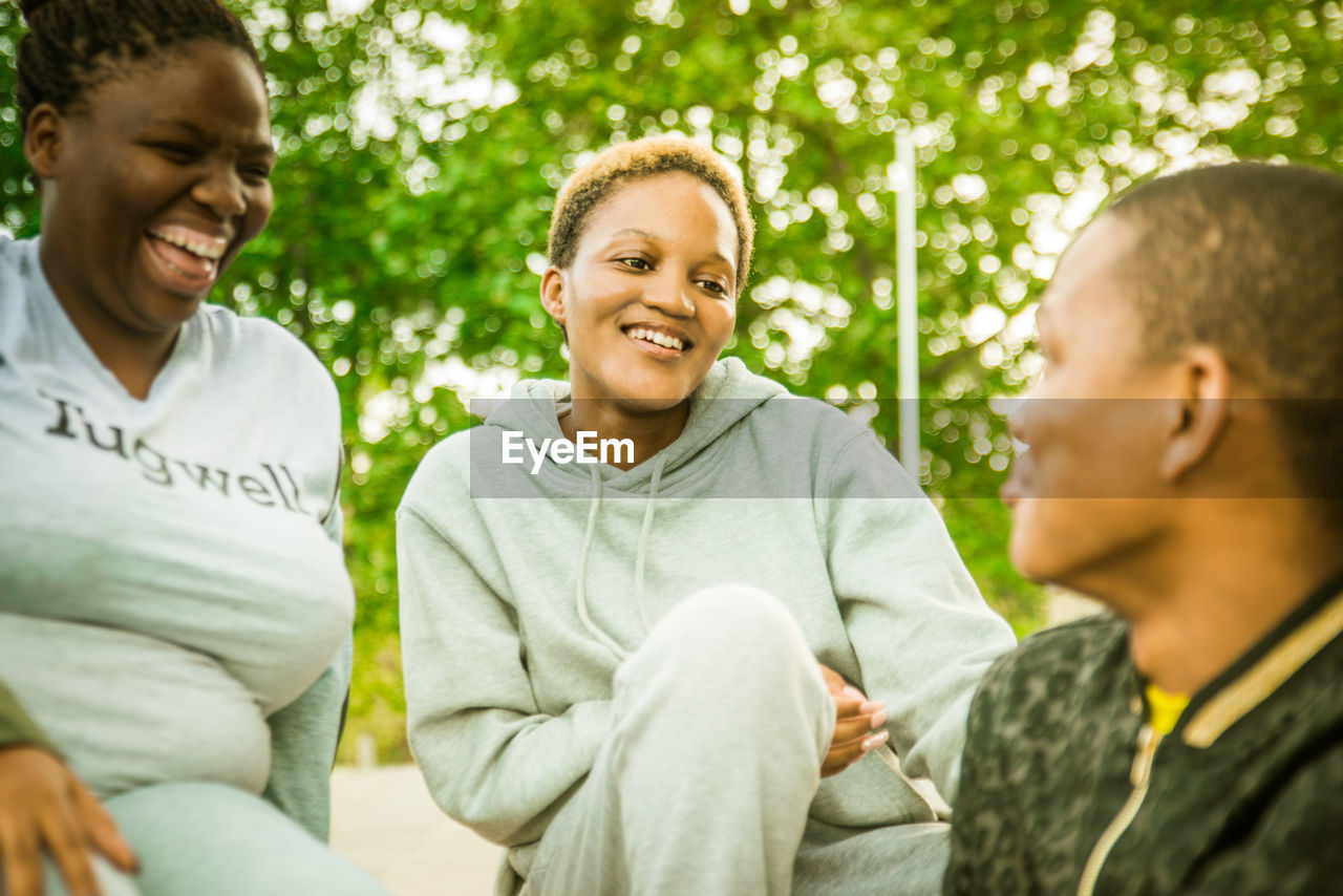 PORTRAIT OF HAPPY FRIENDS SITTING OUTDOORS