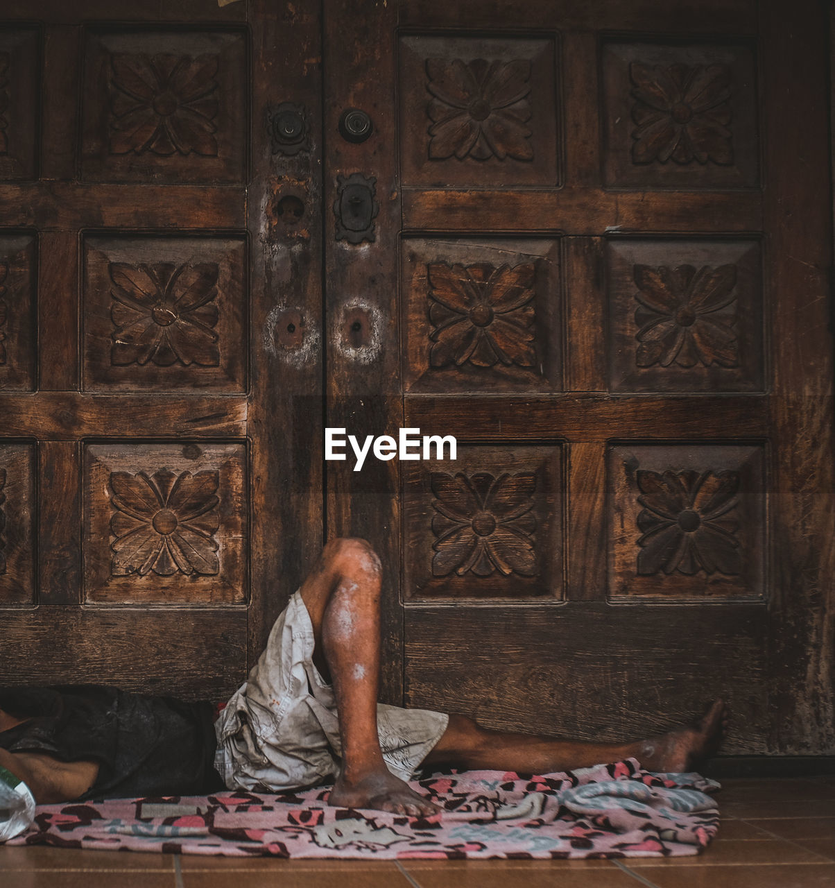 Low section of man sleeping on floor by closed door