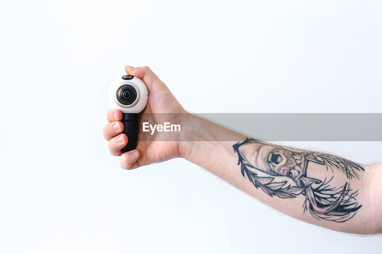 Cropped tattooed hand of man holding camera against white background