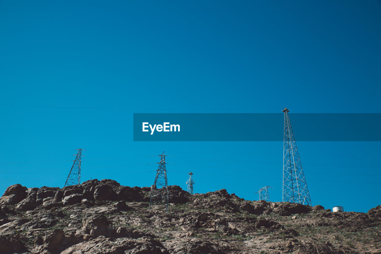 Low angle view of electricity pylons on mountain against clear blue sky