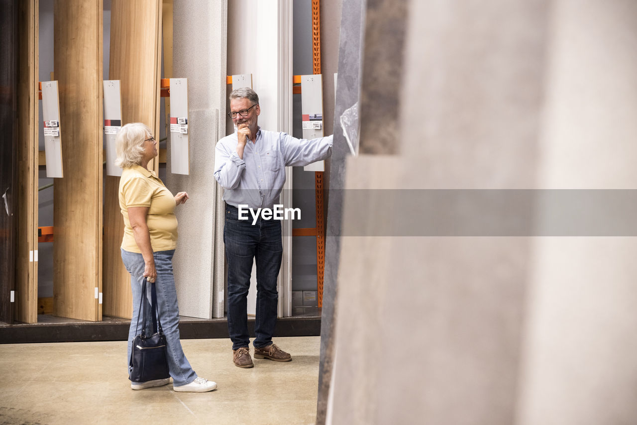 Man with hand on chin looking at woman while choosing laminated boards at hardware store
