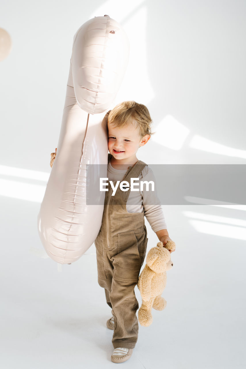 Happy child boy is holding a balloon in his right hand and a teddy bear in his left hand