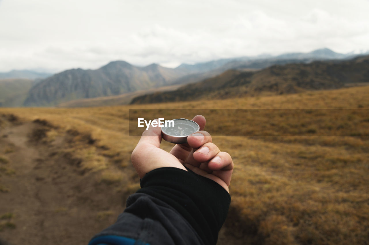 First-person view of a male traveler s hand holding a magnetic compass against the backdrop