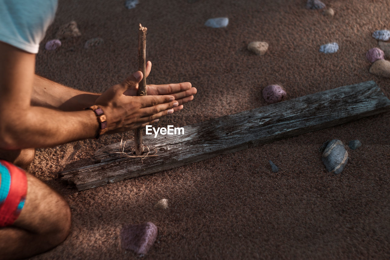 Midsection of man rubbing stick at beach