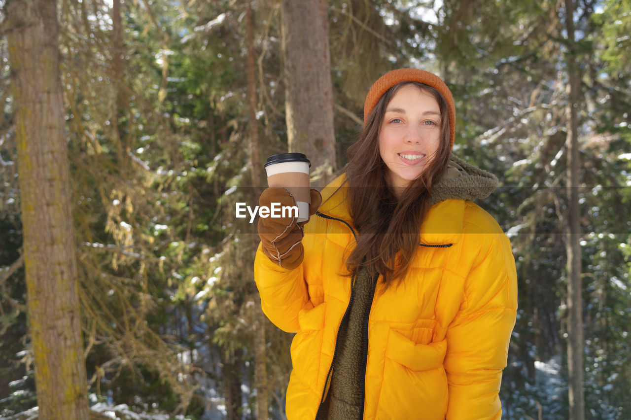 A girl drinks hot tea or coffee in a winter forest from a paper cup