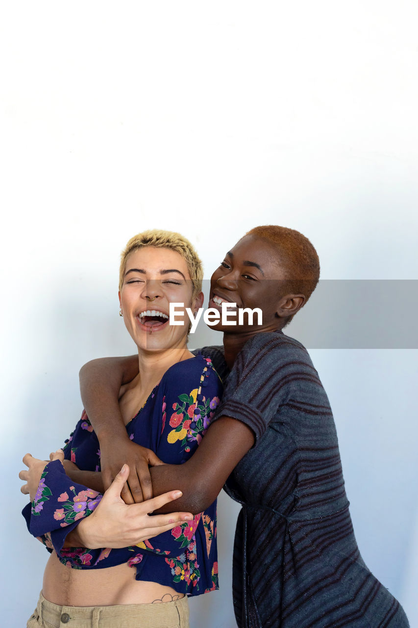 Portrait of cheerful lesbian couple embracing against white background