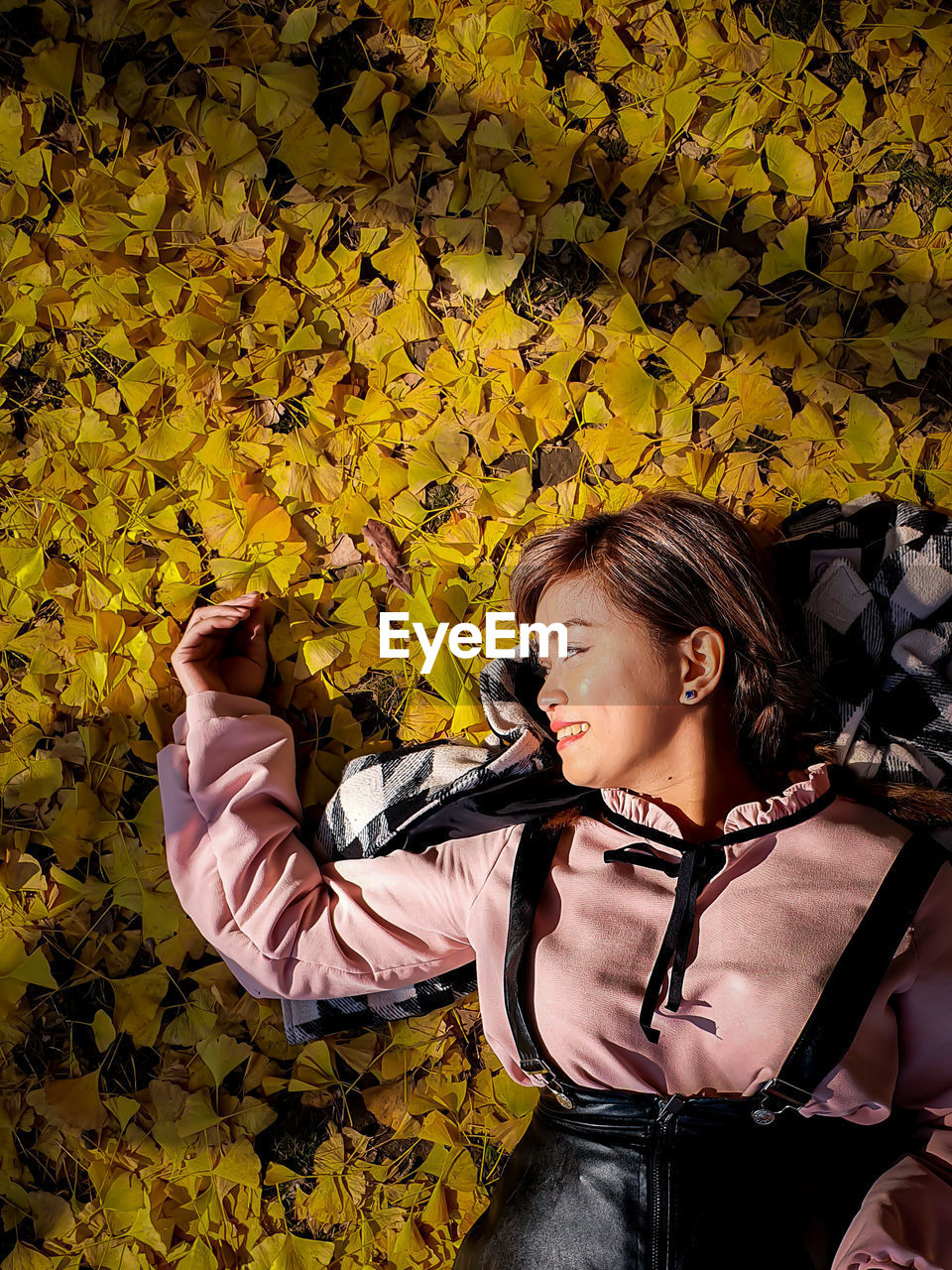 High angle view of smiling woman lying on leaves in park during autumn