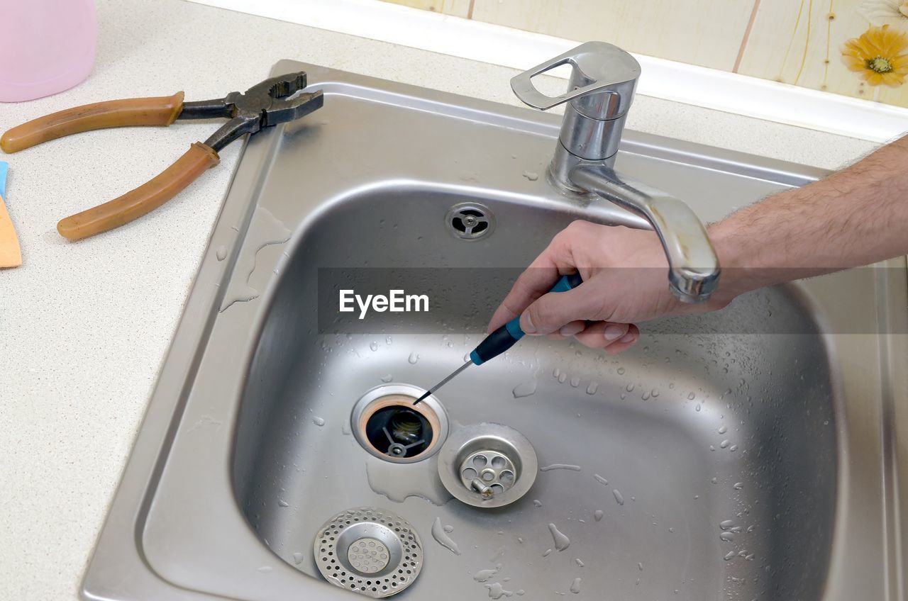 High angle view of man with hand tool cleaning sink in kitchen