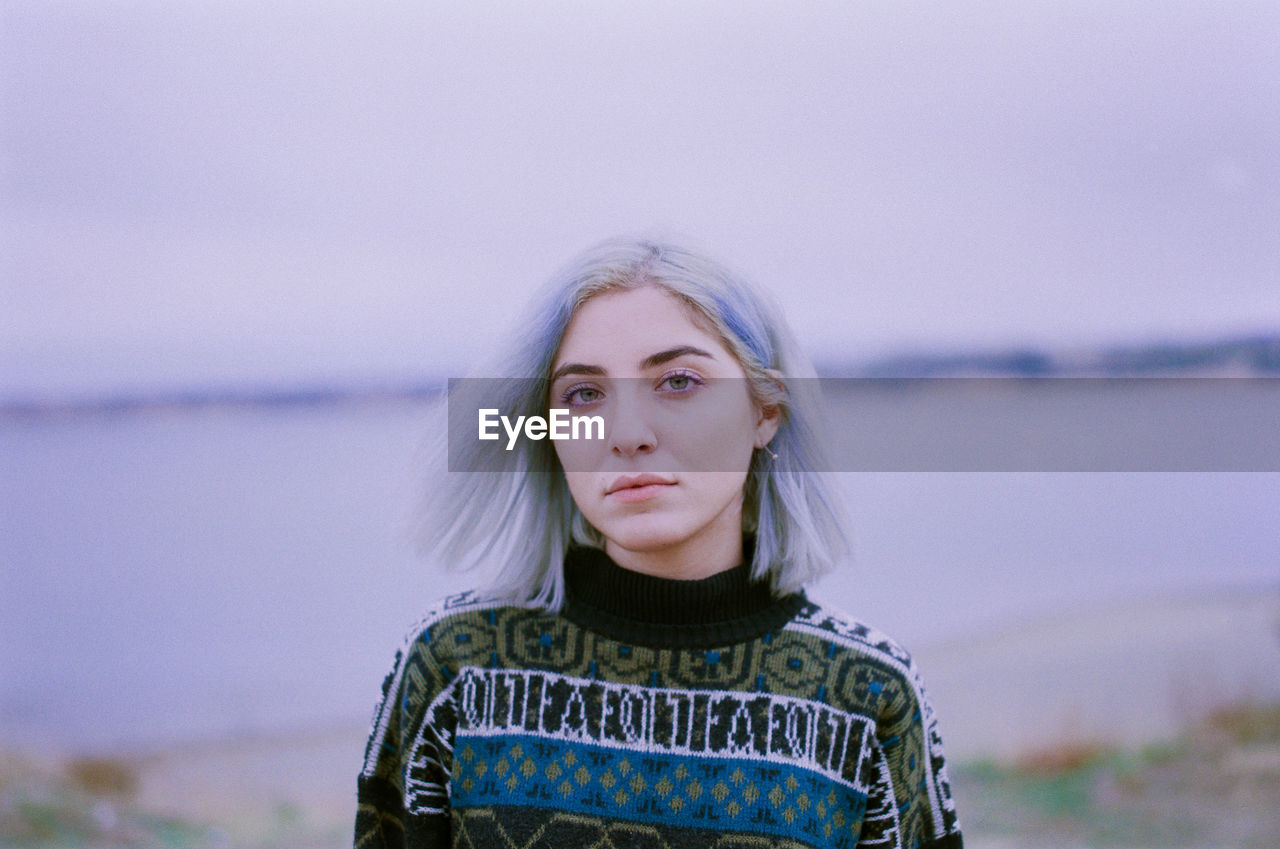 Portrait of beautiful woman with dyed hair standing against lake